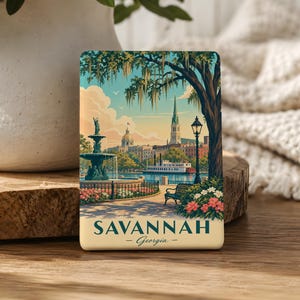 A decorative magnet depicting a scenic view of Savannah, Georgia, with a fountain, trees, and buildings in the background.