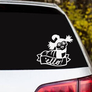 May include: A white vinyl decal applied to a car window featuring a stylized illustration of a worm-like creature with large eyes and hair, positioned above a banner containing the text 'ello!' in a cursive script font.