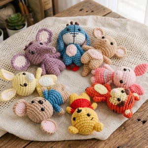 Puede incluir: Una colección de juguetes de personajes de ganchillo hechos a mano en varios colores, incluyendo amarillo, azul, rosa y marrón. Los juguetes están dispuestos sobre una tela color crema y una superficie de madera. Los juguetes parecen estar inspirados en personajes de dibujos animados populares.