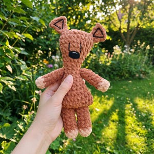 Peut inclure: Un jouet en peluche crocheté de couleur marron avec une surface en fil texturé, doté de deux oreilles pointues avec des coutures triangulaires noires, un nez brodé noir et des accents beige clair sur le bout des bras et des jambes.