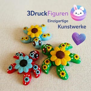 Könnte beinhalten: Bunte, handgefertigte Figuren in Form von Schildkröten und Blumen. Die Schildkröten sind in verschiedenen Farben bemalt, darunter Rot, Blau und Grün, mit Sonnenblumen- und Blumendetails. Der Text "3D Druck Figuren Einzigartige Kunstwerke" ist ebenfalls sichtbar.
