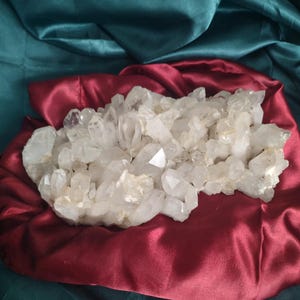 May include: A large cluster of raw, translucent white quartz crystals with sharp, multifaceted points. The mineral formation features numerous individual crystal structures growing together in a dense, irregular arrangement with varying heights and widths.