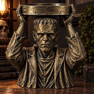 Può includere: Una scultura in resina color bronzo del mostro di Frankenstein, raffigurata dal petto in su, che indossa una giacca logora. La figura tiene un vassoio circolare sopra la testa con entrambe le mani. La superficie ha una finitura metallica.