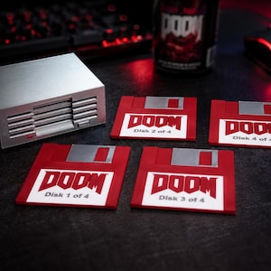 Könnte beinhalten: Ein silbernes Computergehäuse und vier rote Disketten-Untersetzer mit dem Wort "DOOM" in Weiß. Jeder Untersetzer ist mit "Disk" gefolgt von einer Nummer und "of 4" beschriftet. Eine "DOOM"-Dose und eine Gaming-Maus sind im Hintergrund.