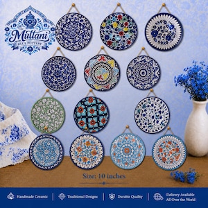 May include: A display of handcrafted, blue ceramic plates featuring detailed floral and geometric patterns. Each plate, about 25 cm in diameter, hangs by a gold-toned string. The image includes the text "The Multani Blue Pottery".