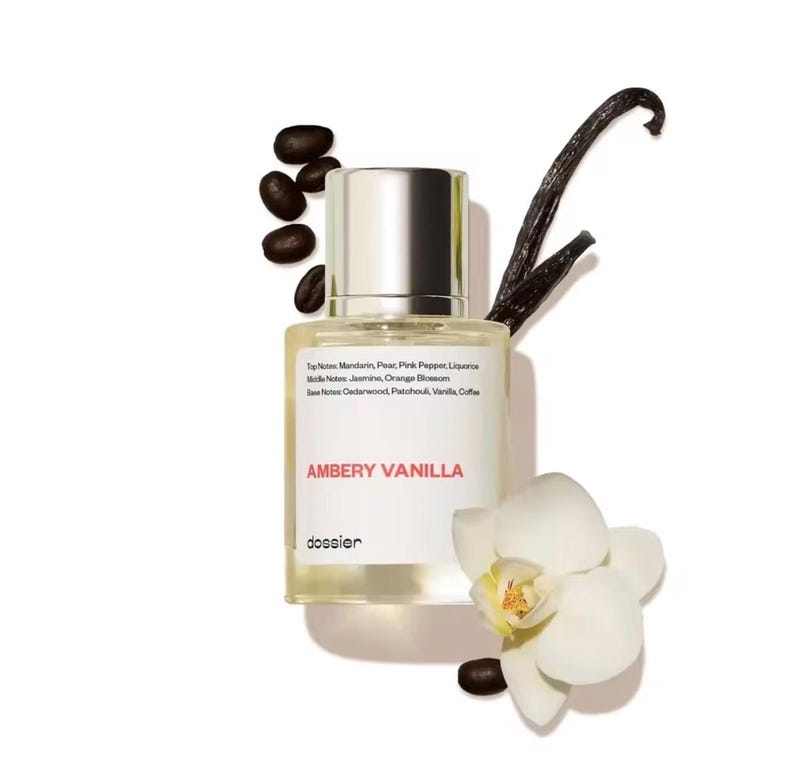 May include: A perfume bottle with a silver cap and a white label that reads "AMBERY VANILLA." The bottle is surrounded by coffee beans, a vanilla bean, and a white orchid. The label lists the top, middle, and base notes of the fragrance.
