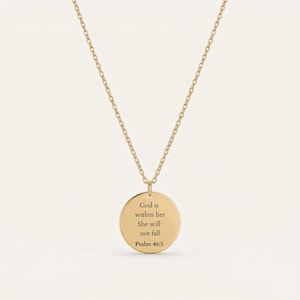 Peut inclure: Un collier doré avec un pendentif circulaire. Le pendentif porte l'inscription "God is within her She will not fall Psalm 46:5" en texte noir. La chaîne est fine et se détache sur un fond clair.