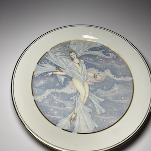 May include: Decorative plate with a celestial design. It features a woman in flowing white fabric, surrounded by stars and clouds. The plate has a gold rim and a cream-coloured border. The artwork is detailed and elegant.