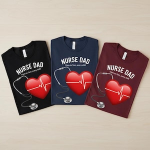 Puede incluir: Tres camisetas en negro, azul marino y burdeos. Cada camiseta presenta el texto "NURSE DAD" sobre un corazón rojo con una línea de ECG blanca y un estetoscopio. El texto "11pm to 7am, every shift" está debajo.