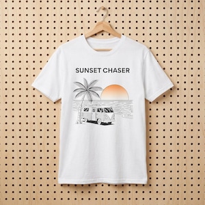 May include: White t-shirt with a graphic design featuring a palm tree, a vintage van, and a setting sun. The text "SUNSET CHASER" is printed above the graphic. The shirt is hanging on a wooden hanger.