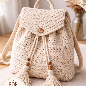 May include: A cream-colored crochet backpack with a flap closure and wooden button. The bag features a drawstring closure with tassels and wooden beads. The text "HÄKELANLEITUNG" is at the top, and "PDF PATTERN" is at the bottom.