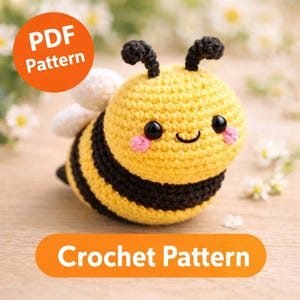 Könnte beinhalten: Gehäkelte Biene mit gelben und schwarzen Streifen, schwarzen Augen und rosa Wangen. Die Biene hat weiße Flügel und schwarze Fühler. Der Text "PDF Pattern" und "Crochet Pattern" ist im Bild enthalten.