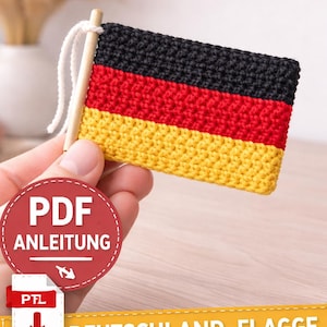 Könnte beinhalten: Eine gehäkelte Deutschlandflagge mit schwarzen, roten und gelben Streifen, befestigt an einem Holzstab. Der Text "Häkelanleitung", "PDF Anleitung" und "Deutschland-Flagge" ist ebenfalls im Bild enthalten.