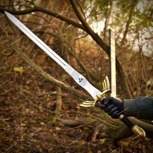 May include: A silver-colored sword with a gold-colored hilt and a black handle. The blade is long and straight, with a triangular emblem near the hilt. The sword is held against a backdrop of trees.