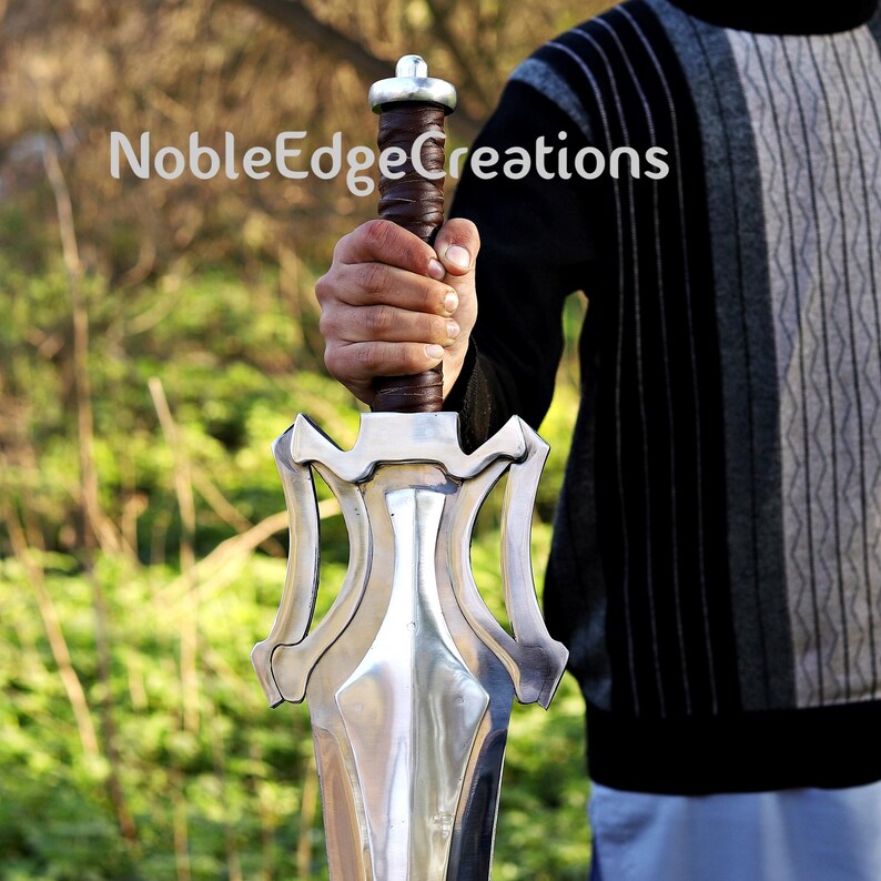 May include: A silver sword with a decorative hilt and a brown leather-wrapped grip. The sword is held in a person's hand. The text "NobleEdgeCreations" is visible in the image.