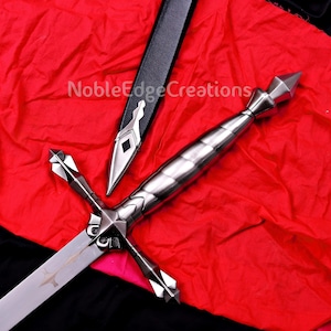 May include: A silver sword with an ornate hilt and crossguard, displayed on red fabric. The sword features a long blade and a black sheath. The text "NobleEdgeCreations" is visible. The sword is likely made of steel.