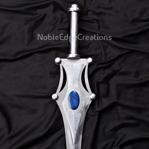May include: A silver-colored sword with a blue oval-shaped gem in the center of the blade. The sword has a long, cylindrical handle and decorative accents. The text "NobleEdge Creations" is printed on the background.