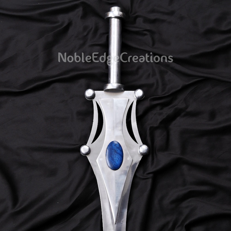 May include: A silver-colored sword with a blue oval-shaped gem in the center of the blade. The sword has a long, cylindrical handle and decorative accents. The text "NobleEdge Creations" is printed on the background.