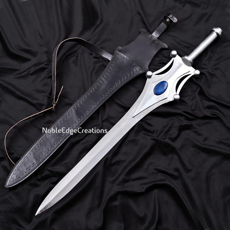 May include: A silver sword with a blue gem in the center of the hilt, resting next to a black leather sheath. The sword has a decorative handle and a long, sharp blade. The sheath has a strap and is embossed with a pattern. The text "NobleEdgeCreations" is visible.
