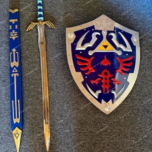 May include: A prop sword, shield, and scabbard set. The sword has a gold hilt and blade, with a blue and teal handle. The shield is blue with silver trim and red and gold accents. The scabbard is blue and gold.