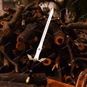 May include: A decorative sword with a silver blade and a black handle. The sword features gold accents on the hilt and a gold pommel. The sword is displayed against a backdrop of stacked logs.
