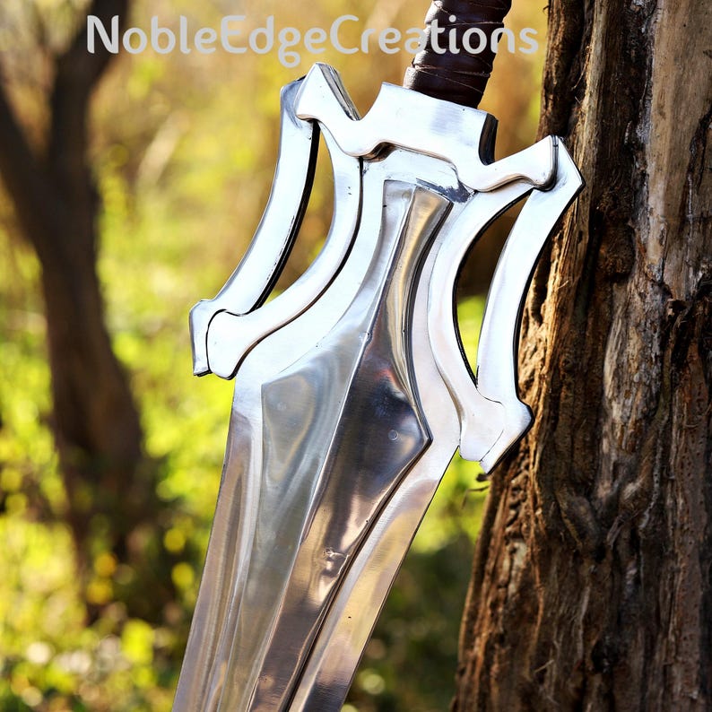 May include: A shiny silver sword with a brown leather-bound handle. The blade features an unusual, angular design with decorative cutouts near the hilt. The text "NobleEdgeCreations" is visible at the top of the image.