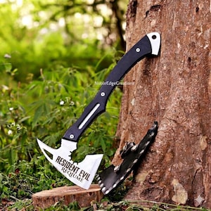 May include: A black and silver axe with the text "RESIDENT EVIL REQUIUME" on the blade. The axe is leaning against a tree trunk, with a black sheath nearby. The handle is black with silver accents.