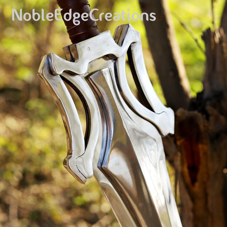 May include: Close-up of a polished metal sword with a brown leather-wrapped handle. The sword has a decorative hilt with curved, stylized elements. The text "NobleEdgeCreations" is visible at the top.
