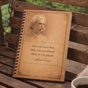 May include: A notebook with a sepia-toned cover featuring a portrait of Mark Twain and a quote. The notebook rests on a wooden bench with a pillow and a cup of coffee. The quote reads: "Get your facts first, then you can distort them as you please."