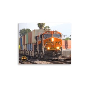 May include: An orange BNSF freight train hauling shipping containers. The train is on a track with the number 3257 visible on the front. The containers are various colors, including blue, brown, and beige.