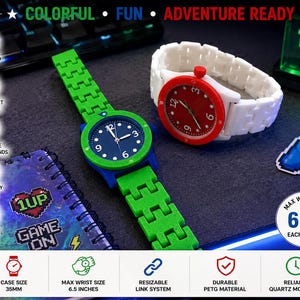 May include: Two colorful watches with a gaming theme. One watch has a green band and blue face with white numbers, the other has a white band and red face. The watches are next to a notebook and a controller sticker. The max wrist size is 6.5 inches.