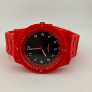 May include: A bright red wristwatch with a black watch face. The watch has a red band and a round red bezel. The watch face displays white numerals and hands. The watch is water resistant.
