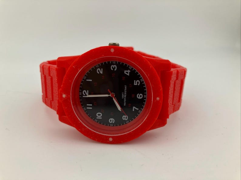 May include: A bright red wristwatch with a black watch face. The watch has a red band and a round red bezel. The watch face displays white numerals and hands. The watch is water resistant.