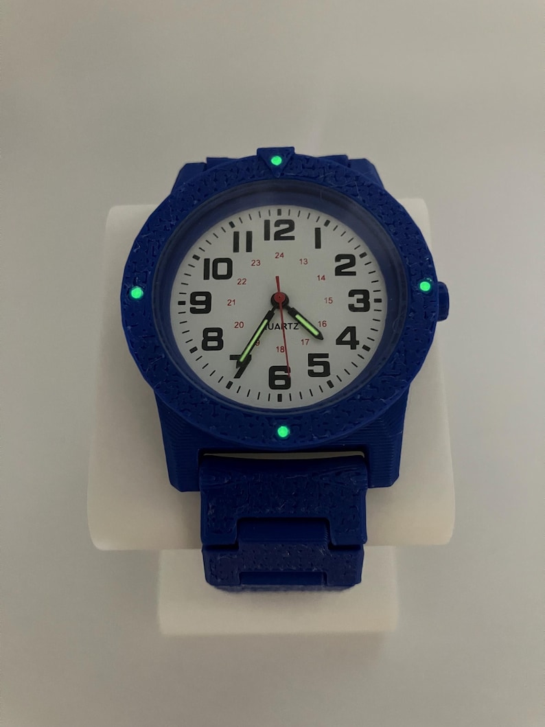 May include: A blue quartz watch with a white face, black numerals, and luminous green markers. The watch has a textured bezel and band. The watch face displays the word "QUARTZ".