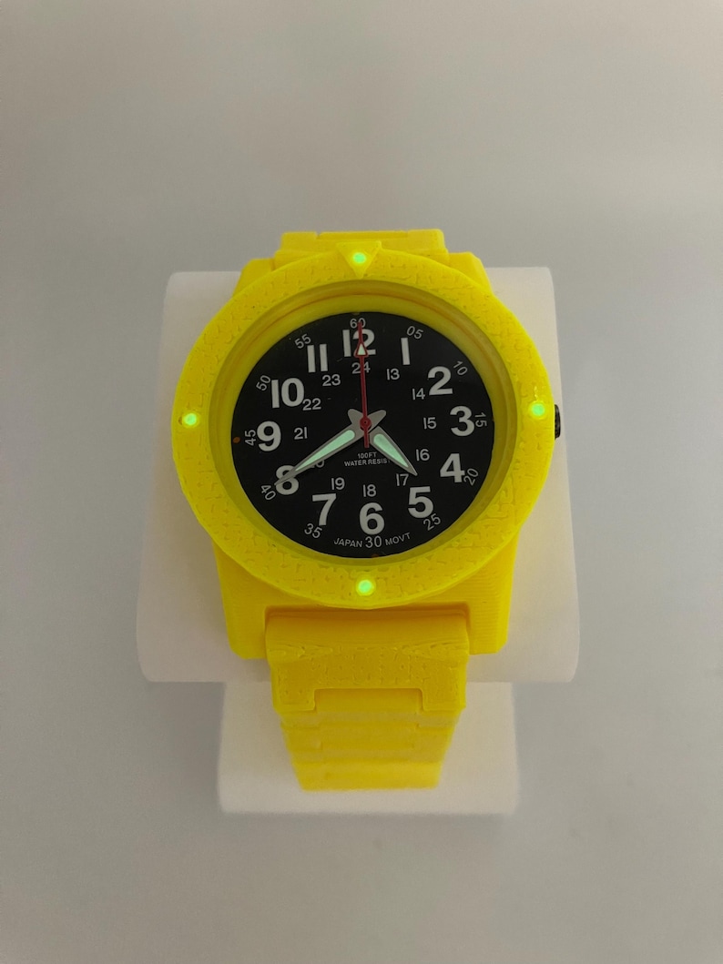 May include: A bright yellow wristwatch with a black watch face. The watch has white numerals and hands, with a red second hand. The watch band is also yellow. The watch is displayed on a white stand.