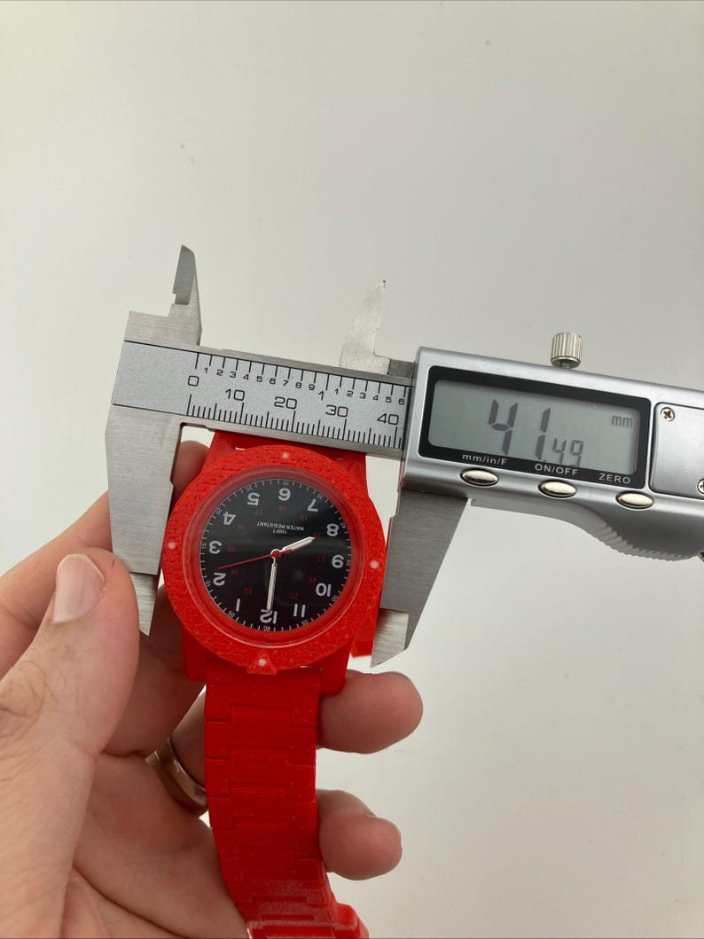 May include: A red wristwatch with a black face is measured with a digital caliper. The watch face displays white numerals and hands. The caliper reads 41.49 mm, approximately 1.63 inches.