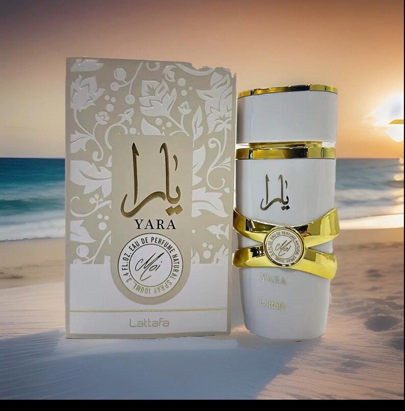 Puede incluir: Un frasco de perfume blanco con detalles dorados y la palabra "YARA" en escritura dorada, junto a una caja a juego. La caja presenta el mismo texto y dise&ntilde;os florales. El frasco contiene 100 ml de perfume.