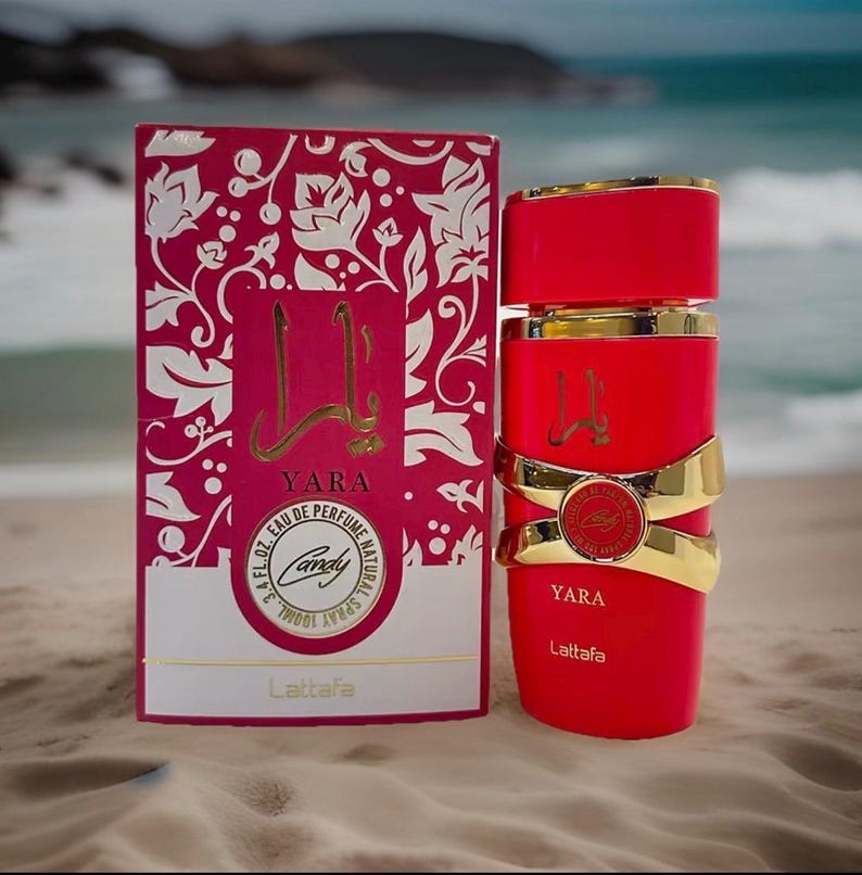 Puede incluir: Un frasco de perfume rojo con detalles dorados y una caja a juego. La caja es rosa con un dise&ntilde;o floral blanco y la palabra "Yara" en dorado. El frasco es cil&iacute;ndrico con bandas doradas y el nombre "Yara" en dorado.