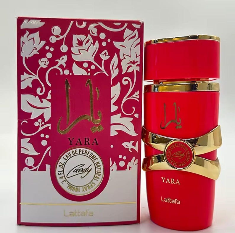 Puede incluir: Un juego de botella y caja de perfume rojo. La botella tiene detalles dorados y la palabra "Yara" en escritura dorada. La caja es rosa con un dise&ntilde;o floral y las palabras "Yara" y "Candy" son visibles. La botella contiene 100 ml.