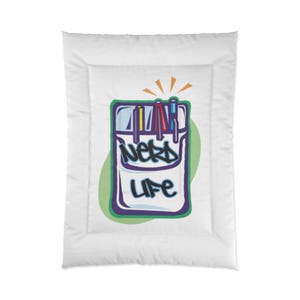 Może przedstawiać: Biała kołdra z kolorową grafiką piórnika. Piórnik ma słowa "NERD LIFE" w kolorze niebieskim i białym, z zieloną i fioletową obwódką. Widoczne są trzy długopisy.