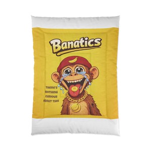 Puede incluir: Un edredón con fondo amarillo que presenta un mono de dibujos animados con gorro rojo y cadena dorada. El mono está llorando y tiene un plátano en la boca. También se ve el texto "Banatics" y "There's nothing curious about this".