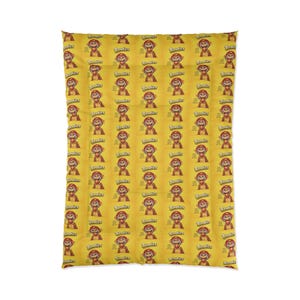 Puede incluir: Un edredón amarillo con un patrón repetido de un mono de dibujos animados con un sombrero rojo y la palabra "Banities". El edredón tiene un aspecto suave, ideal para un dormitorio.