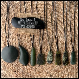 Puede incluir: Una colección de ocho collares de jade en cordones negros, con diversas formas que incluyen círculos, medias lunas y rectángulos. Una etiqueta rectangular de arpillera muestra el texto: New Zealand & British Columbian JADE NECKLACES.