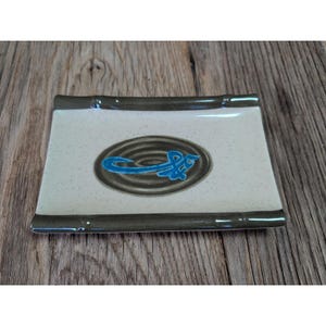 May include: A white ceramic mug with a black handle and the text "But First, Coffee" in a bold, black font. The mug is set against a blurred background, suggesting a cozy setting.