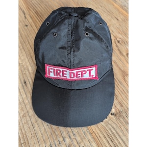 Op de afbeelding: Zwarte baseballcap met een gebogen klep. De cap heeft de tekst "FIRE DEPT." in witte letters op een rood en wit rechthoekig embleem. De cap heeft drie kleine ventilatiegaten.