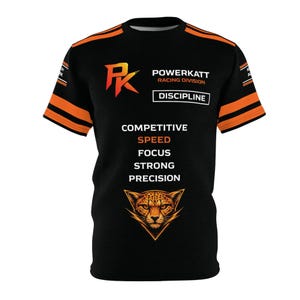 Puede incluir: Camiseta negra con detalles naranjas y texto. La camiseta presenta el logotipo de Powerkatt Racing Division, la palabra "DISCIPLINE" y las palabras "COMPETITIVE SPEED FOCUS STRONG PRECISION". Un gráfico de guepardo en la parte inferior.