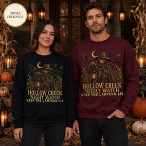 Puede incluir: Una sudadera negra y una granate con cuello redondo, cada una con un espantapájaros sosteniendo un farol en un campo de maíz bajo una luna creciente. El texto dice HOLLOW CREEK NIGHT WATCH KEEP THE LANTERN LIT. Son modelos de cuello redondo unisex.