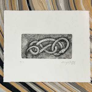 May include: A monochrome etching print depicting a snake in an infinity knot. The artwork is on white paper with a deckled edge. The print is signed and numbered 7/10. The background features a marbled pattern.