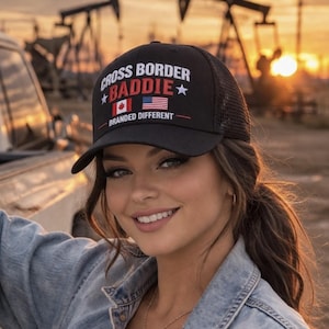 May include: Black trucker hat with the text "CROSS BORDER BADDIE" in white, with a Canadian flag and an American flag. The hat also has the text "BRANDED DIFFERENT" in red. The hat is worn by a person.
