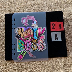May include: A translucent planner dashboard featuring a colorful graphic with the text NAIL BOSS. The design includes illustrations of a hand, nail polish bottles, a nail file, scissors, a mirror, and flowers in pink, yellow, and blue tones.